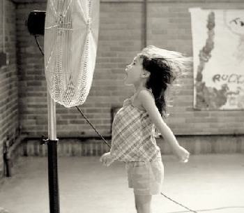 Little girl cooling off in front of a fan.